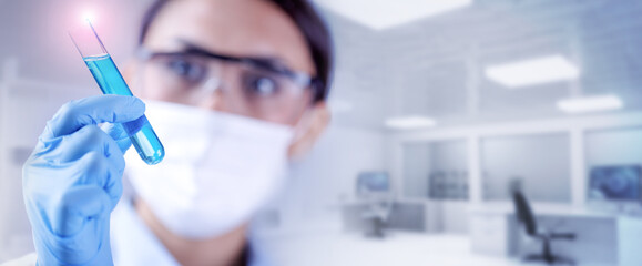 Blurred female scientist holding a test-tube filled of blue liquid sample in chemical lab. Concept of biochemistry, pharmaceutical or medical research