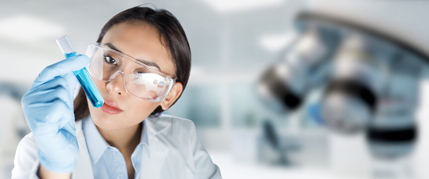 Female lab technician wearing glasses and gloves analyzes a test-tube in laboratory. Chemistry, pharmaceutical or biotechnology research concept.