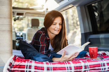 Senior woman inside camper van  reading a book and drinking coffee - Focus on face