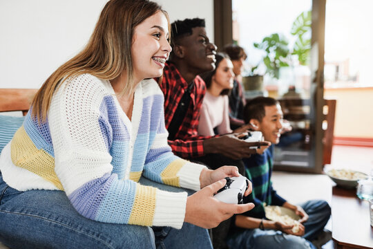 Multiracial young friends having fun playing video games at home - Focus on girl hand holding controller