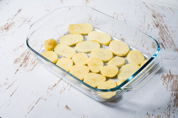 Potato bed in a glass baking dish to prepare a chicken cava in the oven with potatoes