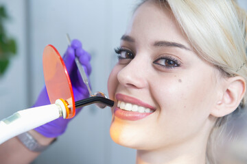 Female patient with a beautiful smile during a dental procedure with a UV lamp