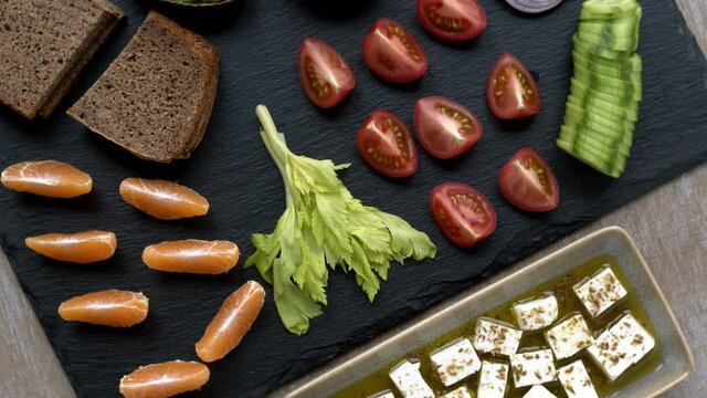 Assortment of fresh healthy snacks vegetables, fruits, guacamole and spiced cheese cubes with bread on black slate. Table spin.