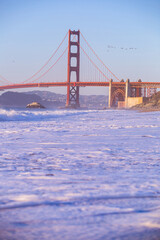 Golden Gate Bridge viewed from the beautiful Baker Beach with the waves crashing on the sand on a sunny day with blue skies, San Francisco, California, USA.