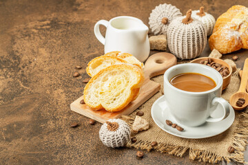 Breakfast concept with a cup of coffee, croissants, milk jug, and decorative crochet pumpkins