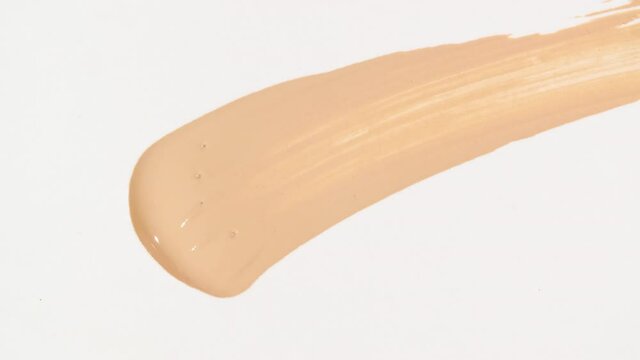 Macro shot and slow motion of a brush, applicator, smear, concealer isolated on white background. Advertising professional cosmetics. Closeup of a cosmetic liquid foundation or cream beige color. 4k