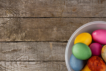 Rustic Easter background with a cup of bright festive eggs, top view, place for text, flat lay and copy space.