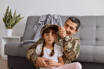 Indoor shot of happy family enjoying meeting, young adult soldier man wearing camouflage uniform returning home after army, spending time with daughter, comes back home.