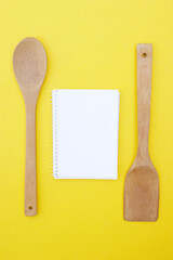 A set of bamboo dishes and blank notebook on a bright yellow background.