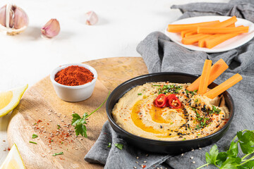 Delicious hummus in ceramic bow lwith  carrot stick dipped in hummus. Colorful snack composition on a white background.