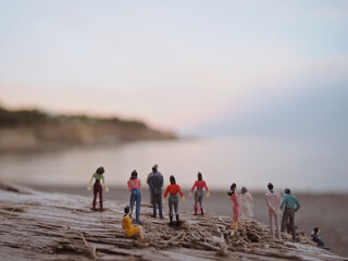 Miniature figures of different kind of people in front of the sea at the sunrise