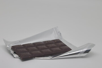 A bar of chocolate lies on a shiny silver wrapper, a delicacy sweetness