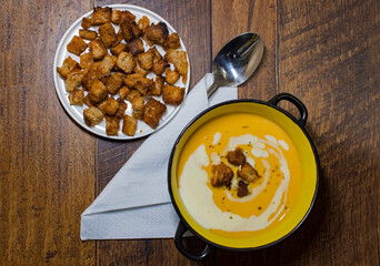 Pumpkin cream soup garnished with croutons on wooden brown background