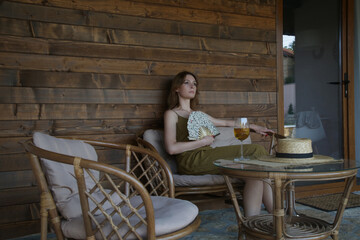 Young woman enjoying a glass of wine on the cozy wooden balcony during summer afternoon	