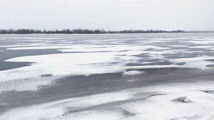 Snow river winter landscape. Frozen ice and snow by river. Spring thawed ice on water.
