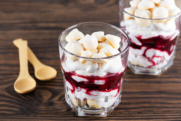 Homemade dessert with aquafaba meringue, coconut cream and cherries in glasses on a brown wooden table. Sugar, lactose free, vegan.