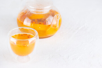 Sea buckthorn tea with orange juice in a glass and teapot on the table. Horizontal orientation, copy space.