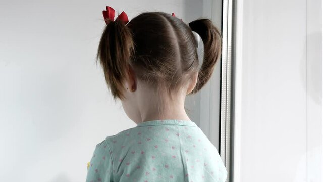 A Little Girl With Two Tails Sits With Her Back To The Camera And Plays, The Child Is Offended, The Crisis Of Three Years, Children's Tantrums.