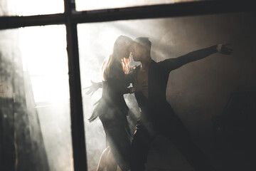 Couple of two professional ballroom dancers is dancing on loft studio. Beautiful art performance with heavy smoke. Sport life concept. Passion and emotional dance.