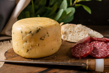 A small spiced cheese piece on a board with bread and salami.