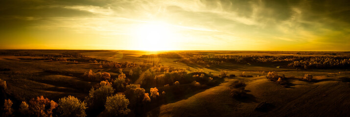 Aerial panorama of a sunset over the gentle rolling hills of the Great Plains with trees in their...