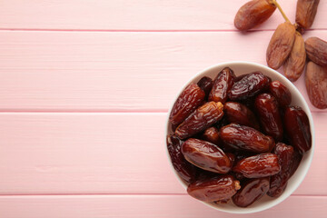 White bowl of dried dates on pink background.