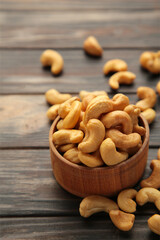 Cashew nuts on wooden bowl on brown background. Top view. Vertical photo.