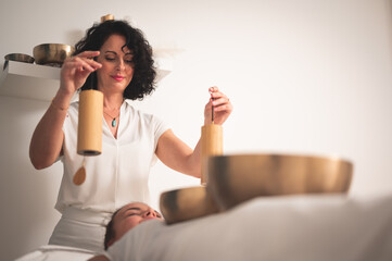 Caucasian female therapist  holding Koshi chime musical  instrument over young woman's head on...