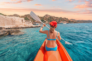 Happy girl is rowing on a sea kayak near Kekova island with view of Simena Castle and Kaleucagiz village in Turkey. Outdoor recreation and exploration. Travel as a lifestyle