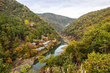 The Katsura River flowing outside of Kyoto Japan with some buildings along the shoreline in fall.