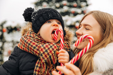 Happy mother and little child with Christmas candies, at the Christmas fair, happy family on the background of the city