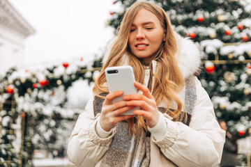 Cute and happy woman using mobile phone outdoors in the city, typing text messages on smartphone...