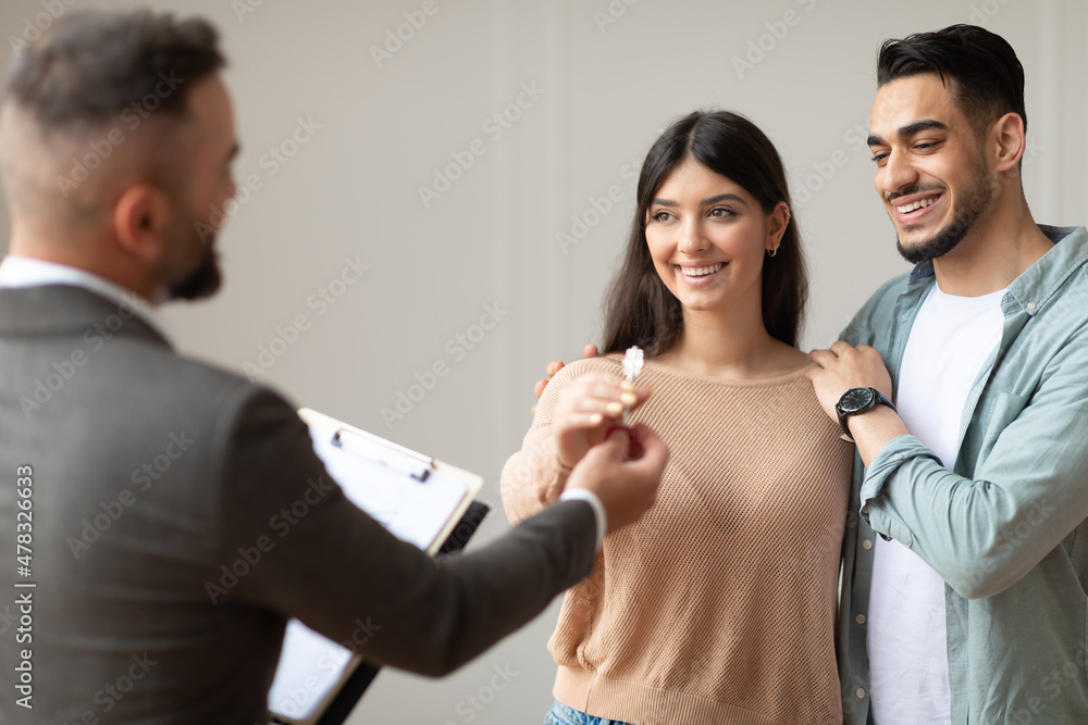 Poster real estate agent giving keys to happy arab buyers