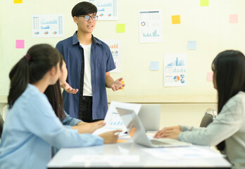 Young man presenting work to team with data graph on whiteboard.