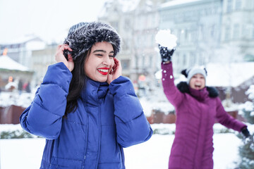 Happy friends play snowballs in winter. Two cheerful women are having fun time together