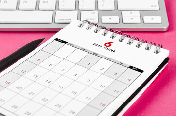 June 2022 desk calendar with pencil on pink background.