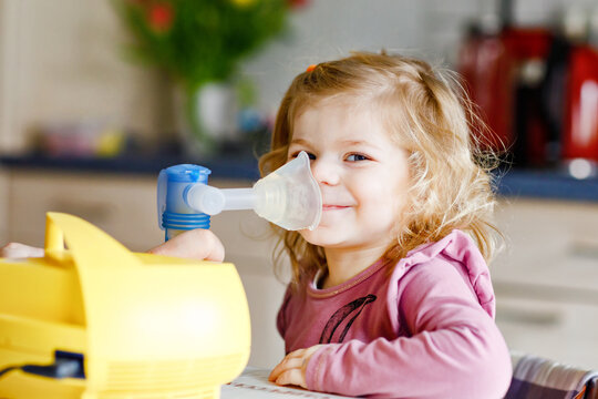 Little toddler girl making inhalation with nebulizer at home. Father or mother helping and holding the device. Child having flu, cough and bronchitis. asthma inhaler inhalation steam sick concept