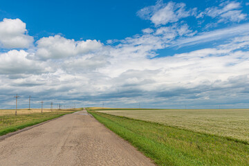 A wide road stretching into the distance and against the backdrop of endless fields and hills on a summer day.