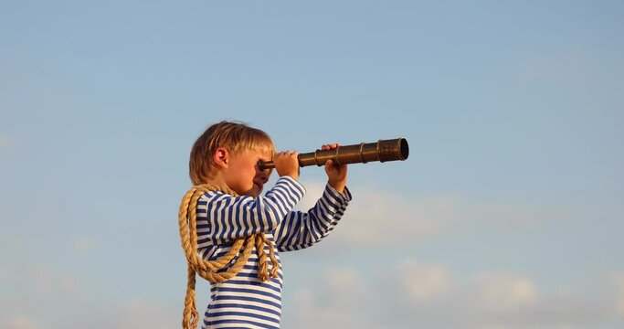 Kid with telescope having fun outddor against blue summer sky. Explore and discovery concept. Slow motion