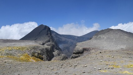 Summit crater of Mount Etna volcano in Sicily, Italy. Yellow Sulphur (Sulfur) deposits on the gray and brown rocks. Blue sky with white clouds.