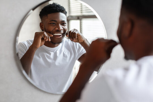 Black guy flossing teeth with tooth floss near mirror indoor