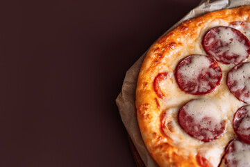 Whole pizza with salami on brown background.