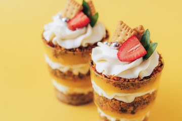 Puff cupcakes with strawberries and cookies in glasses on yellow background.