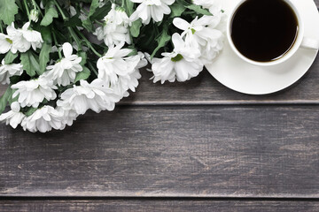 A bouquet of chrysanthemums and a white cup with coffee on a wooden table with a place for text. Background Banner