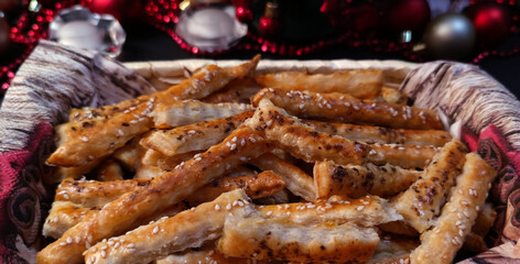 Close-up view of puff pastry salty sticks sprinkled with cumin and sesame seeds in a wicker basket, with Christmas decorations in the background