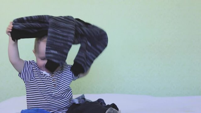 A small child throws clothes around in the bedroom. Concepts of prohibition, rules of conduct, punishment, washing clothes, organizing storage, order, anger, fun, experience, exploration, tactility