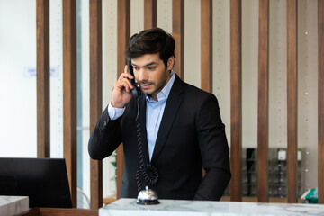 Handsome male receptionist is talking to a tourist who is making a online booking over the phone