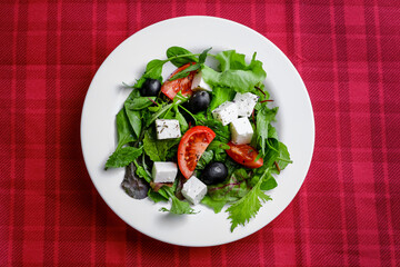 Fresh Greek salad in white plate on red background. closeup and top view.