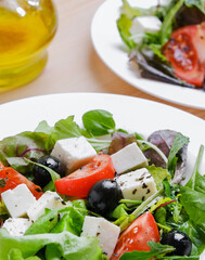 Fresh Greek salad in white plate at wooden table background. Closeup top view.