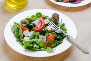 Fresh Greek salad in white plate at wooden table background. Closeup top view.
